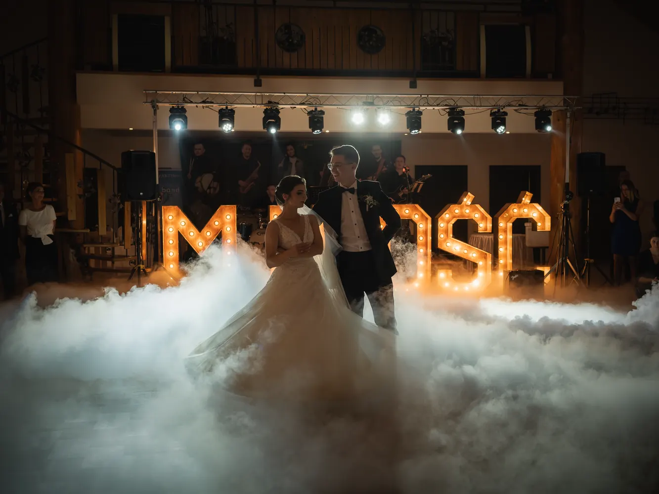 Pierwszy taniec w dymie przed świetlnym napisem, w tle zespół